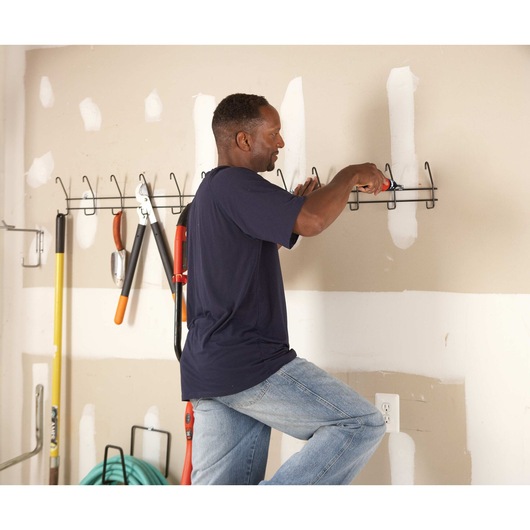 Cordless screwdriver being used by a person to drive screw on a wall.