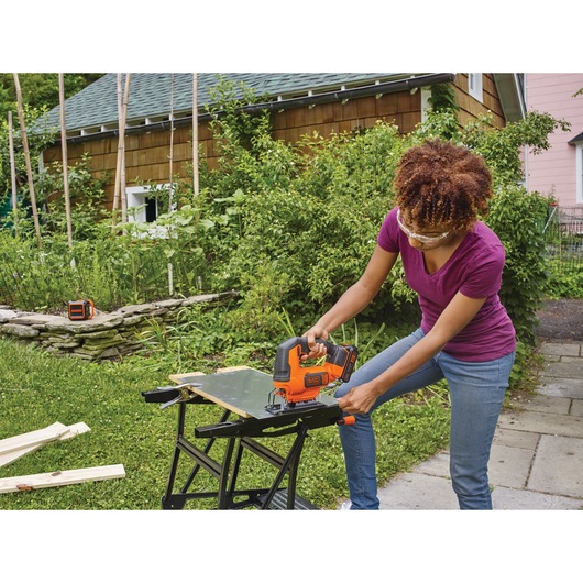 Cordless Jigsaw being used by person to cut thin metal sheet outdoors.