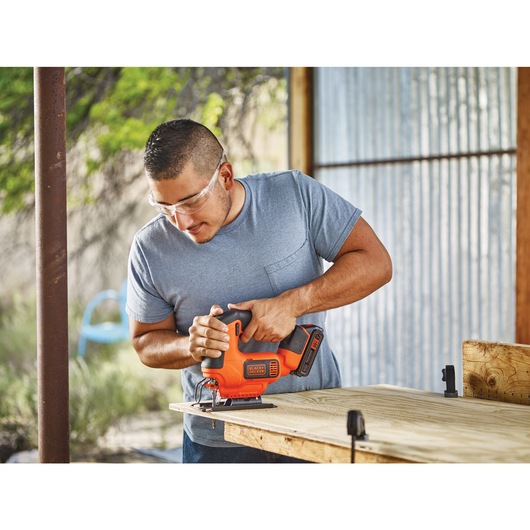 Cordless jigsaw being used by a person to cut wooden sheet.