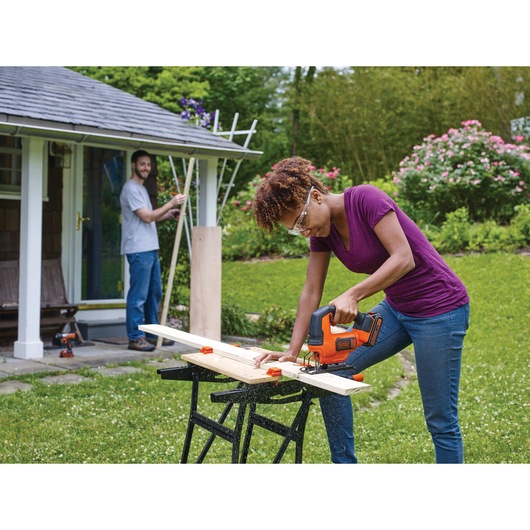 Cordless Jigsaw being used by person to cut plywood for a project in collaboration with another person in home garden environment.