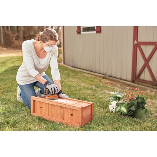 20 Volt Cordless Random Orbital Sander being used by a person on wooden box.