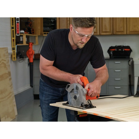 13 Ampere circular saw with laser being used by a person to cut wood.