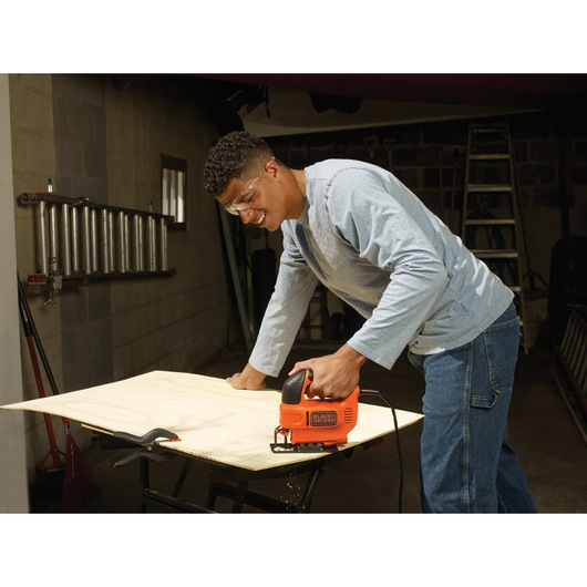 4 and 5 tenths Amp Jigsaw being used by person to cut thin wooden sheet at work place.