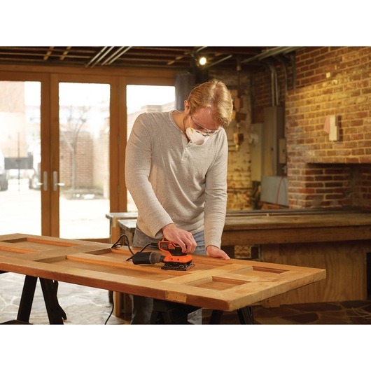 1 quarter sheet orbital sander with paddle switch actuation being used by a person to sand wooden door.