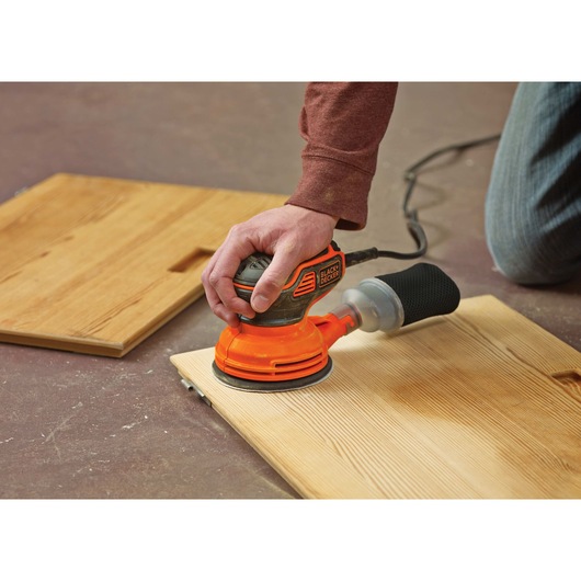 5 inch random orbital sander being used to sand a wooden sheet.