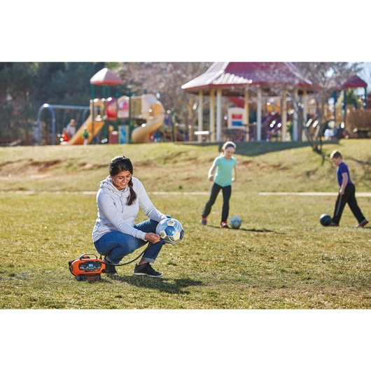 MAX Multi Purpose Inflator being used by person to inflate football in playground.