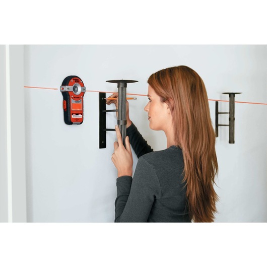 BullsEye Auto Leveling Laser with Stud Sensor being used by person to hang decorative items on wall.