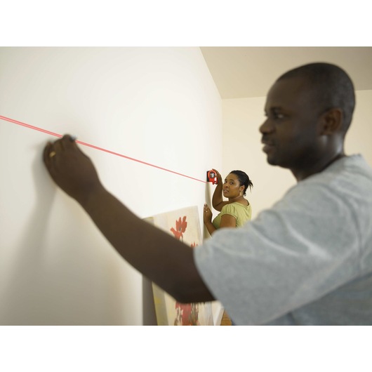 BullsEye Auto Leveling Laser with Stud Sensor being used by two persons to project horizontal laser level line on wall for precise measurement.