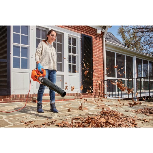 9 amp electric axial leaf blower being used to blow leaves off the house foyer by a person.