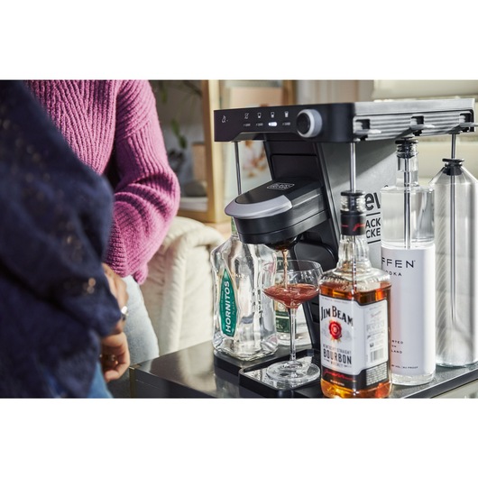 women watching the bev by BLACK+DECKER™ cocktail maker dispense a boulavardier into a coupe glass
