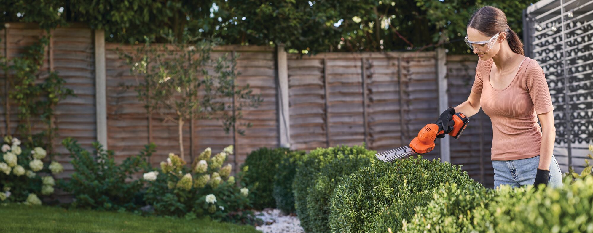 Shear shrubber being used by a person to trim bushes.
