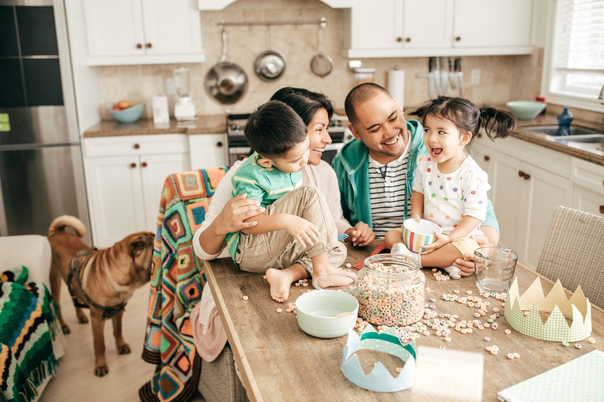 A family sitting in a kitchen smiling over spilled cereal