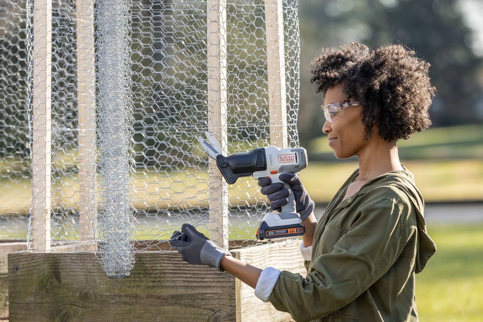 Person cuts chicken wire outside with the BLACK+DECKER MATRIX powered scissors attachment.