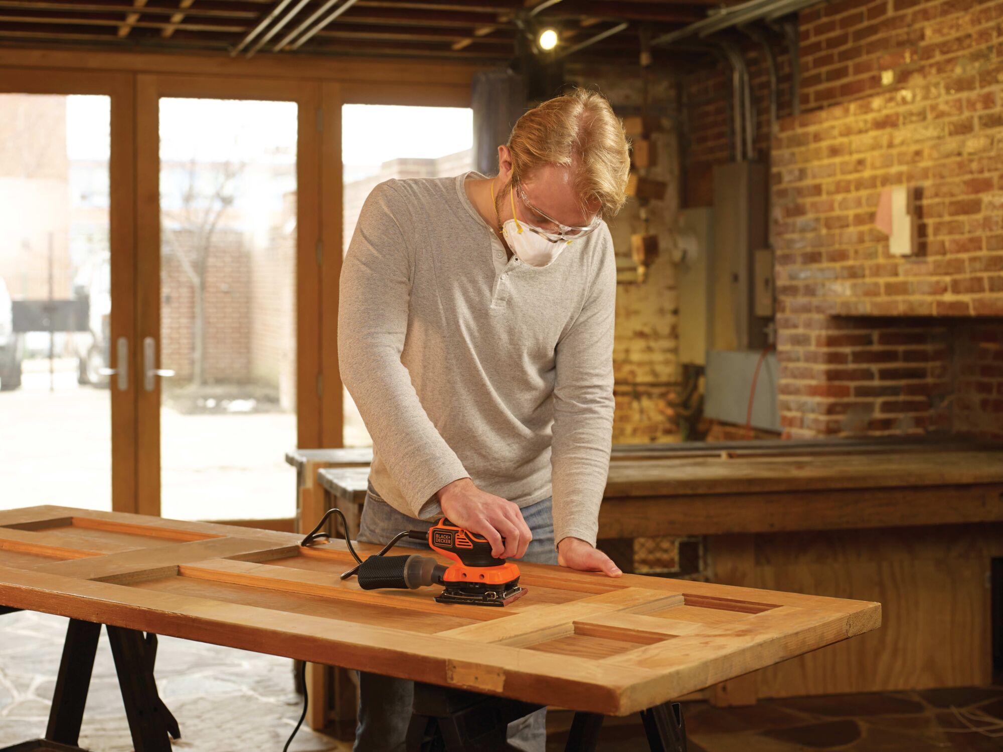 1 quarter sheet orbital sander with paddle switch actuation being used by a person to sand wooden door.
