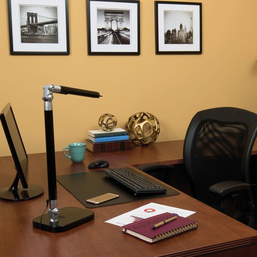 Exalt Bar L E D Desk Lamp placed on wooden desk along with other things in an office space.